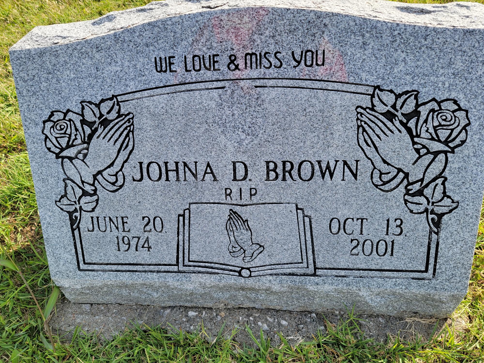 Gravestone with name in center with praying hands and roses on top two corners.